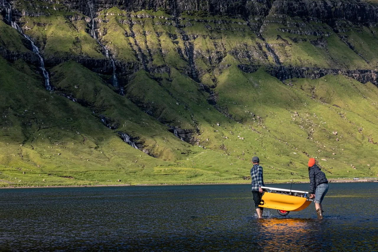 Deux membres de l'équipe BIUTOPIC portent la plateforme autonome HYDRO-01 dans l'eau d'un fjord des îles Féroé