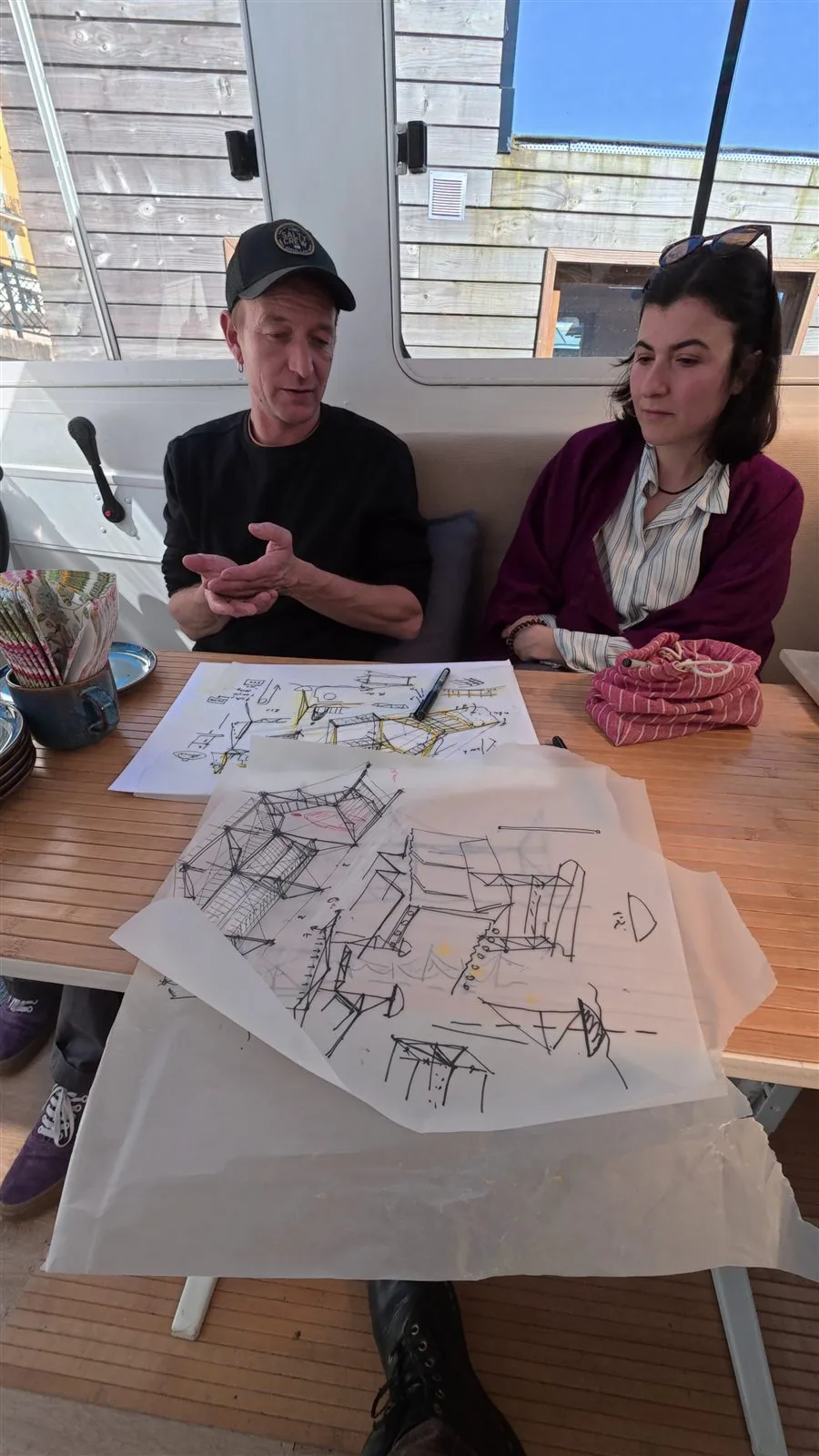 Elven et Claudia en revue de conception de l'exosquelette, croquis étalés à bord de L'Hydronaute